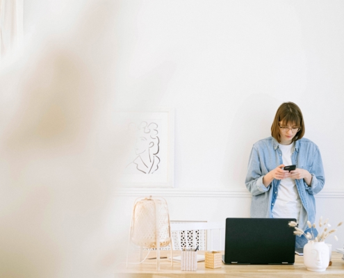 Frau mit Handy vor Laptop