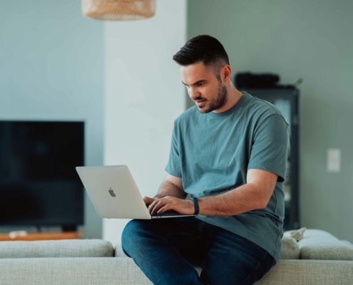 Mann mit Laptop im Wohnzimmer. Tipps für Immobilienmakler auf immowelt impuls zum Thema Suchmaschinenoptimierung für Immobilienmakler.,
